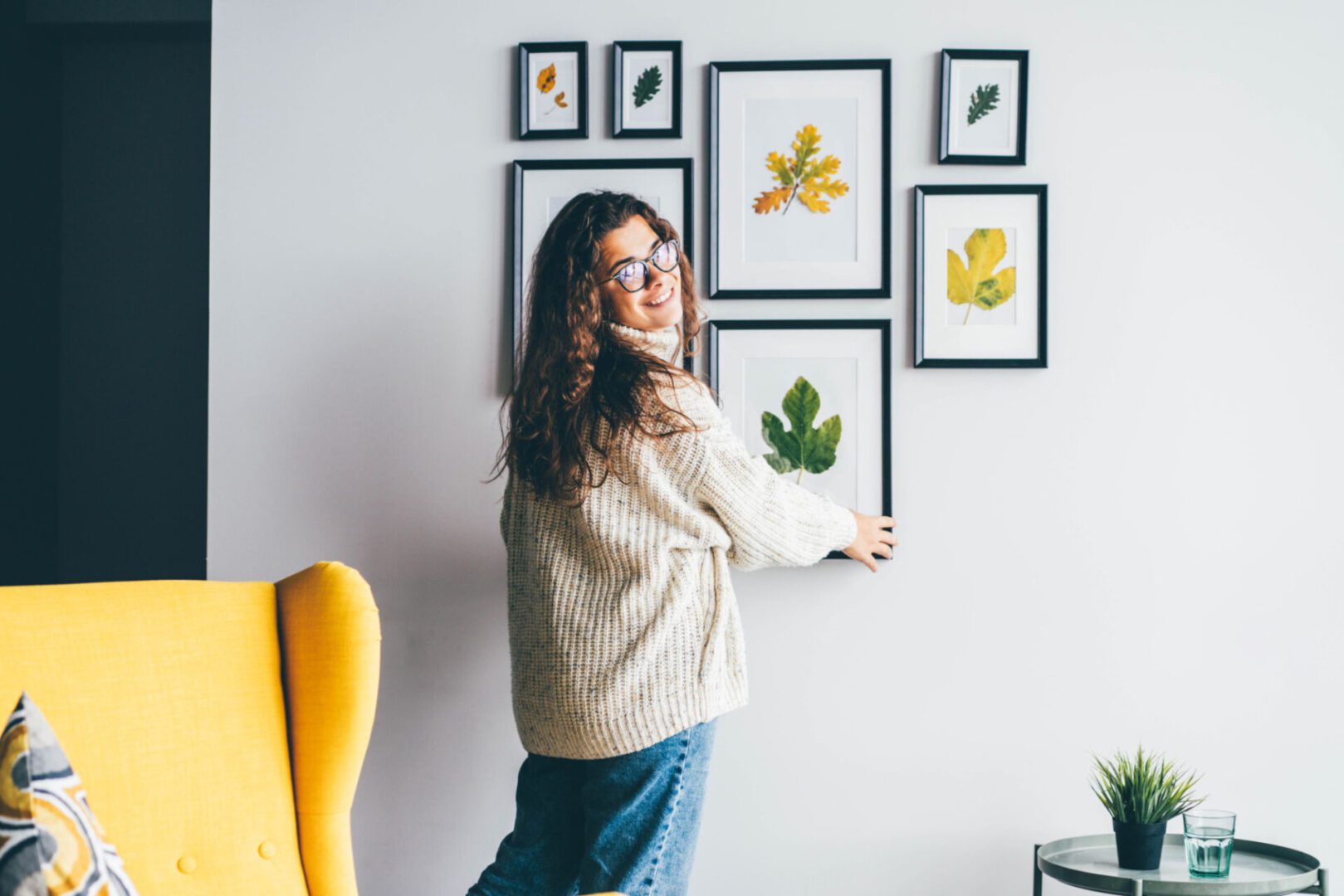 Woman arranging framed botanical art on wall.