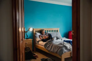 Person relaxing on bed, blue wall background.