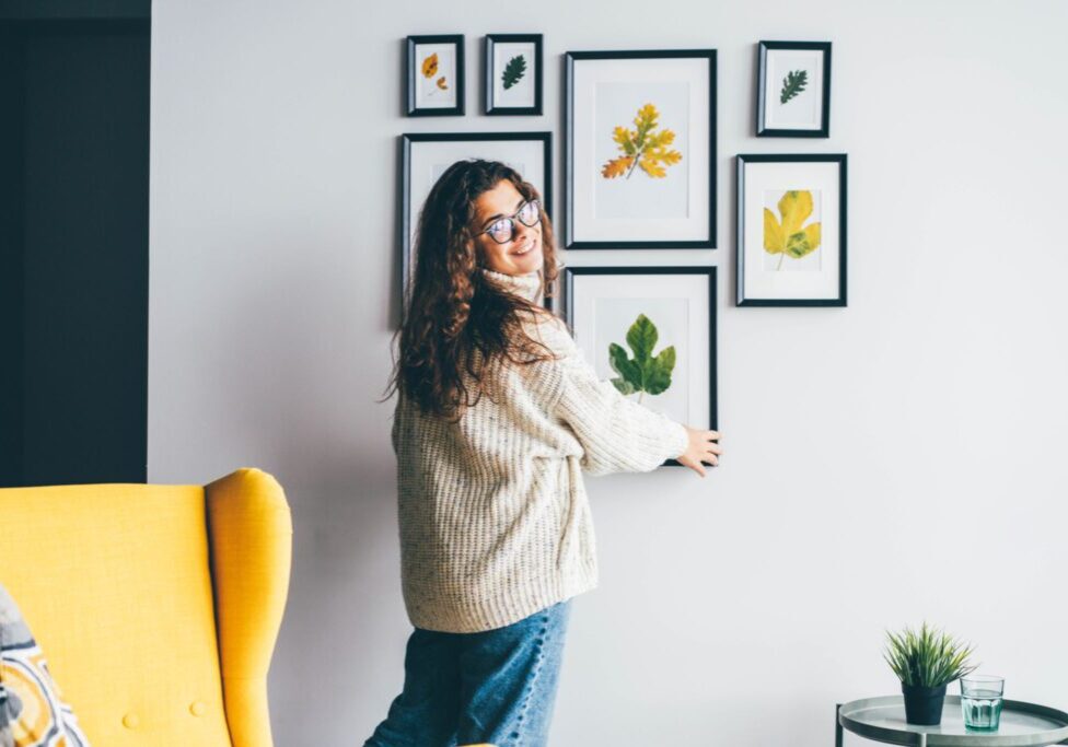 Woman arranging framed botanical art on wall.